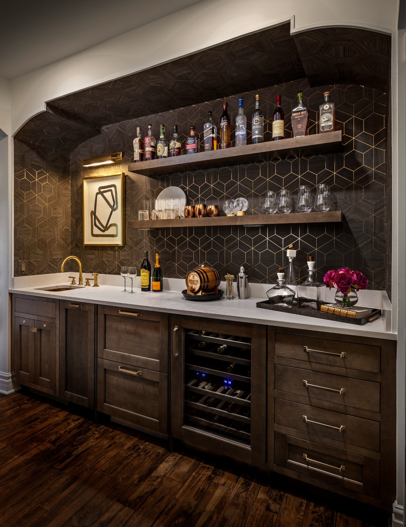 Warm bar and beverage area with dark cabinetry and layered shelving.